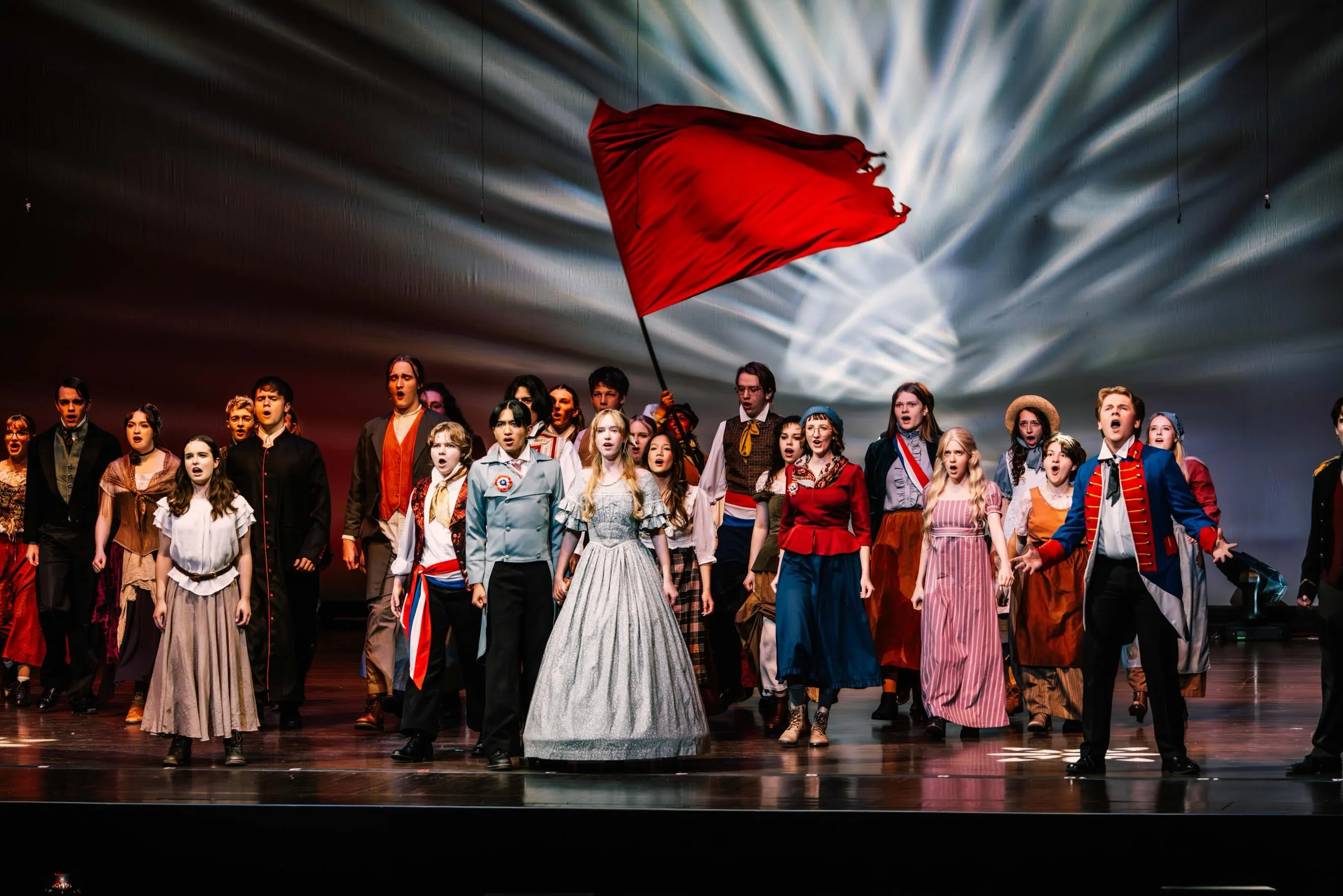 The student cast of Les Misérables performs beneath a red flag