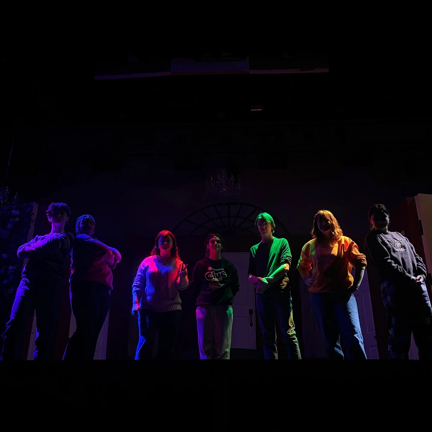 Student performers stand together under colorful stage lighting.