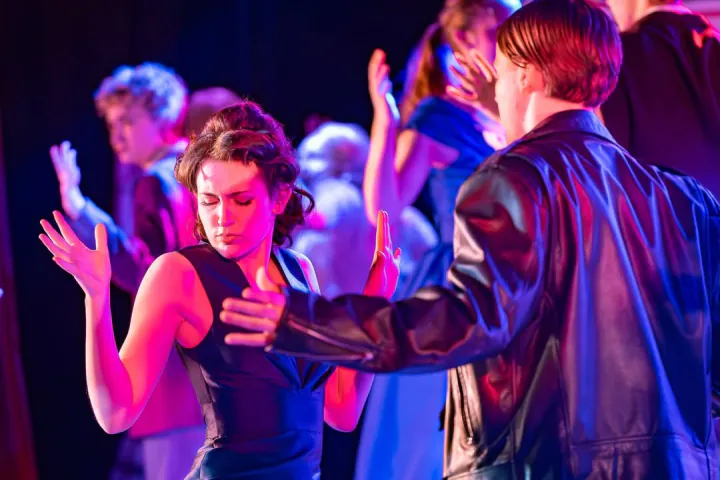 Student performers dance together under vivid pink and blue lighting.