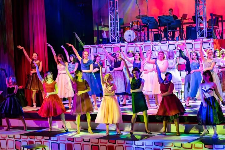 Student performers dance beneath colorful stage lights.