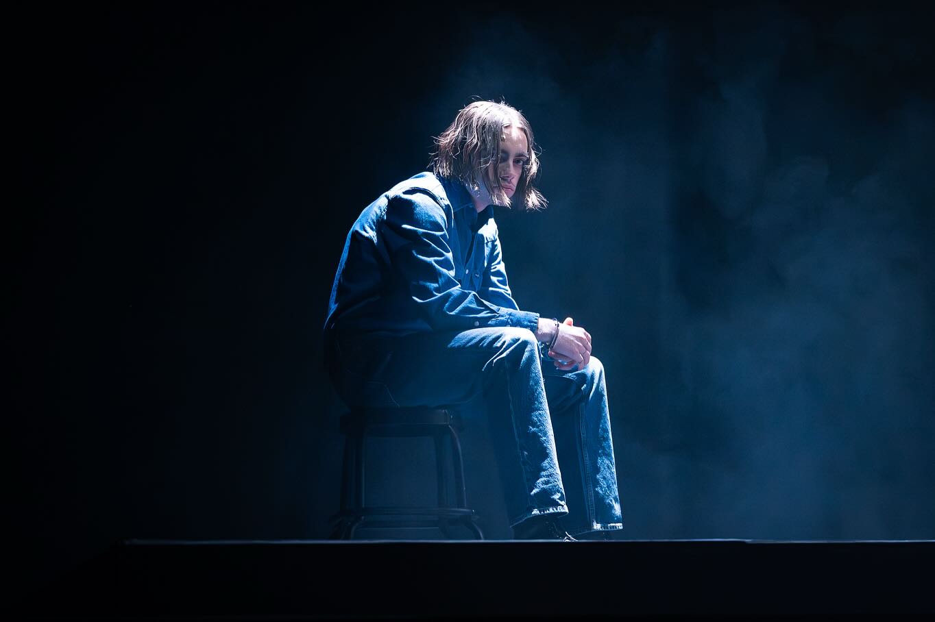 A student actor sits alone in a blue stage spotlight.
